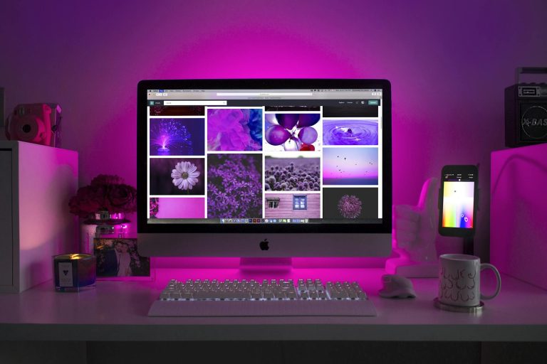 Modern desk setup with neon lighting and a desktop computer displaying colorful images.