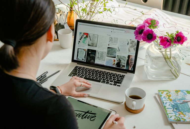 Woman in a creative workspace using a laptop and tablet for calligraphy. Artistic and tech-driven environment.