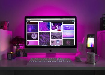 Modern desk setup with neon lighting and a desktop computer displaying colorful images.